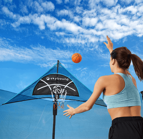 A woman is shooting basketball in to a trampoline basketball hoop from the SkyBound brand.